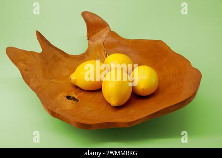 Image minimaliste de nature morte d'un bol en bois contenant des citrons sur un fond vert Banque D'Images