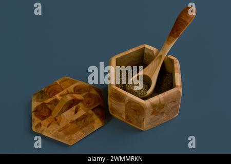 Image minimaliste de nature morte d'une boîte en bois à six côtés contenant du café moulu avec une cuillère en bois et un couvercle en bois sur un fond gris Uni Banque D'Images