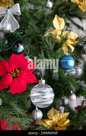 Gros plan de décorations colorées suspendues à un sapin de Noël, poinsettias en velours doré et rouge, rubans fantaisie, boules vintage et lumières fantaisie Banque D'Images