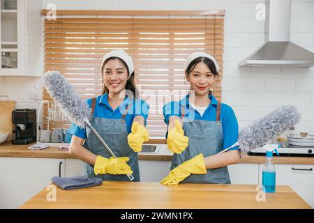 Équipe de nettoyage asiatique deux femmes en uniforme sur le comptoir de la cuisine tiennent le spray brumeux à plumeau et un chiffon Banque D'Images