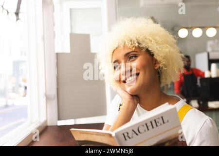 Jeune femme biraciale aime lire à une table de café ensoleillée avec espace de copie Banque D'Images