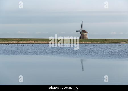 Moulin traditionnel solitaire à toit de chaume au lac Dutch au crépuscule. A moitié caché derrière une digue verdoyante surplombant l'eau tranquille d'une prairie inondée Banque D'Images