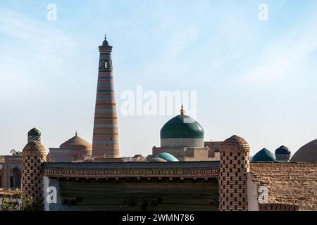 Deux des principales attractions de Khiva (Ouzbékistan) : le minaret Islam Khodja et le mausolée Pahlavan Mahmoud avec un dôme vert unique contre un fond de ciel bleu Banque D'Images