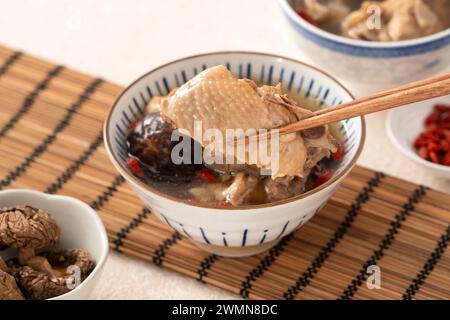 Délicieuse soupe de poulet aux champignons shiitake take taïwanais dans un bol sur fond de table blanc. Banque D'Images