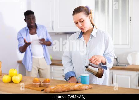 Une jeune femme contrariée verse du café dans une tasse sur fond de mari insatisfait Banque D'Images