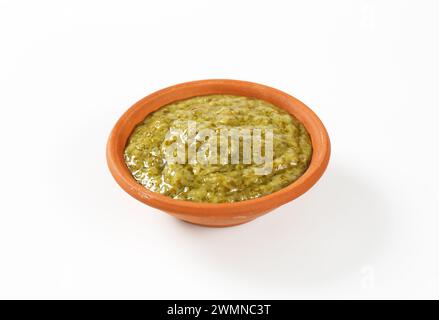 Pesto de basilic dans un bol en terre cuite sur fond blanc Banque D'Images