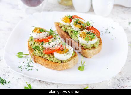 Délicieux pain grillé avec avocat, oeuf dur, tomates et microgreen sur une assiette blanche. Alimentation saine, petit déjeuner. Nourriture Keto Diet. Cuisine tendance. Banque D'Images