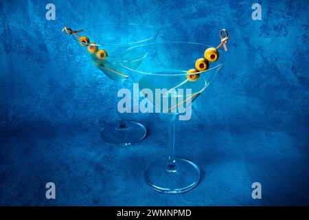 Martini. Deux verres de cocktails martini sales avec vermouth et olives, apéritif, sur fond bleu Banque D'Images