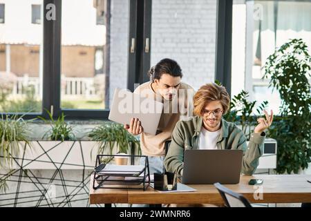 jeune chef d'équipe discutant des détails du projet avec un collègue tout en regardant un ordinateur portable, des hommes dans la vingtaine Banque D'Images