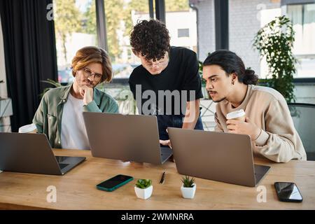 Des jeunes hommes engagés dans la vingtaine analysent le démarrage ensemble sur des ordinateurs portables dans un espace de coworking ensoleillé Banque D'Images