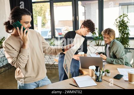 homme souriant ayant un appel téléphonique et regardant des graphiques près de collègues flous brainstorming sur ordinateur portable Banque D'Images