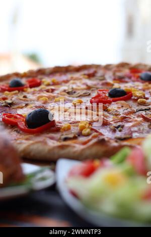 Pizza garnie d'olives noires et de fromage à côté de salade fraîche sur une table Banque D'Images