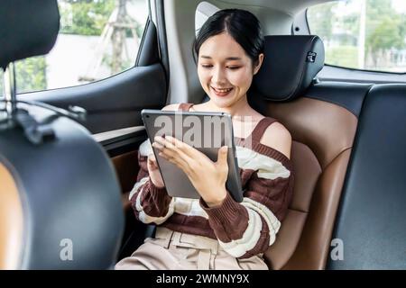 Une jeune femme asiatique utilisant une tablette alors qu'elle était assise dans une voiture. Banque D'Images