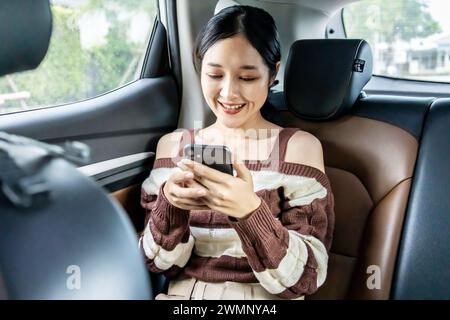 Une femme asiatique dans une voiture utilisant un smartphone. Banque D'Images