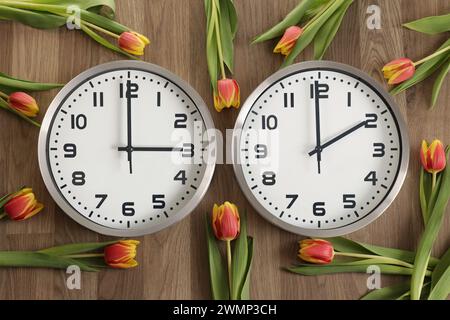 Pour les lecteurs de droite à gauche : deux horloges, l'une indiquant deux heures, l'autre indiquant trois heures. Les tulipes reposent autour. Symbole de changement d'heure. Saveur lumière du jour Banque D'Images