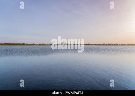 Lac de village hollandais avec prairie inondée. Le ciel passe d'une palette chaude de teintes de coucher de soleil aux tons plus froids qui se reflètent sur la surface des eaux placides Banque D'Images