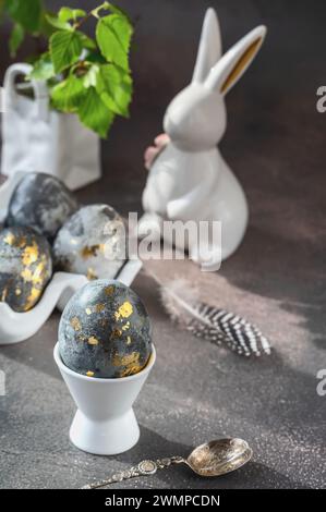 Printemps Pâques nature morte. Lapin blanc et oeufs peints avec un motif doré sur un fond gris.. Décor de Pâques sur la table. Banque D'Images