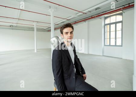 Un jeune garçon est assis sur un tabouret, portant son étui de guitare sur son épaule. Intérieur d'une ancienne usine rénovée. Banque D'Images