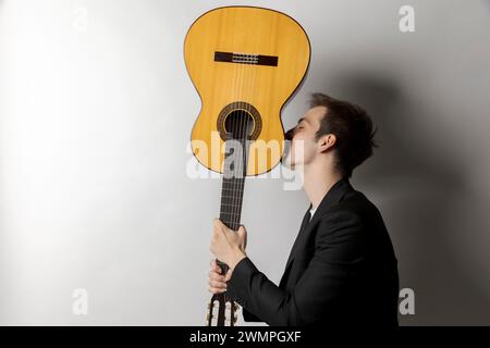 Le jeune garçon tient sa guitare à l'envers et l'embrasse. Isolé sur fond blanc Banque D'Images