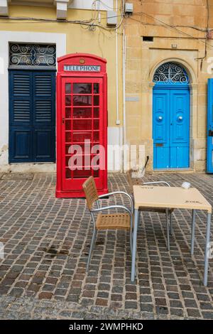 Une vieille boîte téléphonique de style britannique et une porte bleue colorée à Marsaxlokk Square, Marsaxlokk, Malte Banque D'Images