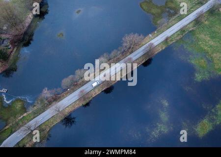 Garlitz, Allemagne. 27 février 2024. Une voiture roule sur une route de district entre deux prairies inondées après de fortes pluies. (Photo aérienne prise avec un drone) de nombreux agriculteurs du nord de l'Allemagne regardent avec une inquiétude croissante leurs champs et prairies, dont certains sont inondés ou au moins trempés. Dans une grande partie de la basse-Saxe, du Mecklembourg-Poméranie occidentale et du Schleswig-Holstein, les agriculteurs ne peuvent actuellement pas utiliser de machinerie lourde sur les sols inondés. Crédit : Jens Büttner/dpa/Alamy Live News Banque D'Images