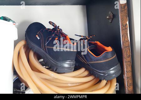 Paire de bottes reposant sur un tuyau orange enroulé à l'intérieur d'une armoire Banque D'Images