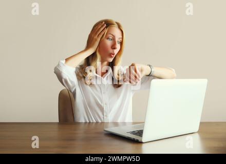 L'employée choquée jeune femme travaillant avec un ordinateur portable regarde la montre, vérifie l'heure, ne parvient pas à terminer un projet sur la date limite assis au bureau dans le bureau Banque D'Images