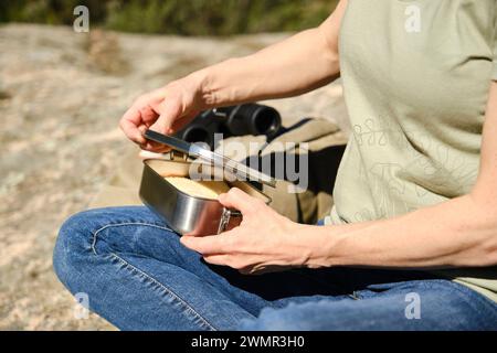 Femme assise ouvrant la boîte à lunch en acier inoxydable dans la forêt Banque D'Images