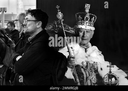 Londres, Royaume-Uni - 22 février 2024 : homme debout devant une affiche du roi Charles III à la gare de Kings Cross à Londres Banque D'Images