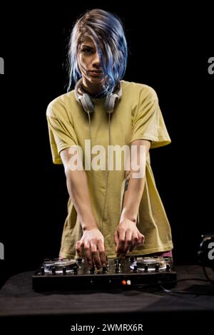 Fille portant des écouteurs se concentre sur le mixage de la musique sur une table d'harmonie. DJ femme avec cheveux bleus et t-shirt jaune. Banque D'Images