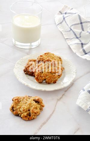 Flocons d'avoine faits maison, raisins secs, bouchées de biscuits aux pépites de chocolat sur une petite assiette avec un verre de lait dans une composition verticale collation nutritive saine. Banque D'Images