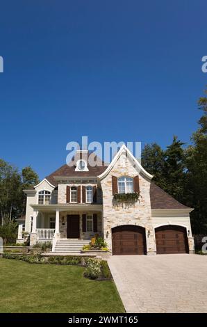 Luxueuse maison en pierre taillée brune et brune de deux étages avec garage pour deux voitures, cour avant paysagée et allée en pierre pavée en été. Banque D'Images