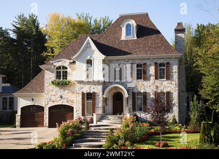 Luxueuse maison en pierre taillée brune et brune de deux étages avec garage pour deux voitures, allée en pierre pavée et cour avant paysagée en été. Banque D'Images