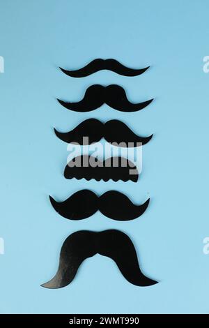 Faux moustaches en papier sur fond bleu clair, pose à plat Banque D'Images