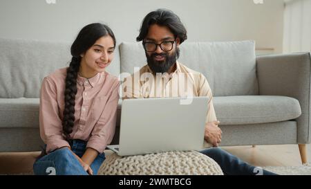 Couple multiracial homme arabe et femme indienne sur le plancher famille couple propriétaires femme petite amie et mari petit ami regardant le film portable Smart TV Banque D'Images