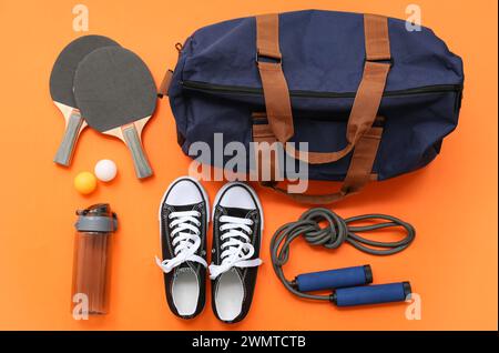 Sac de sport avec vêtements de sport et équipement de ping-pong sur fond orange Banque D'Images