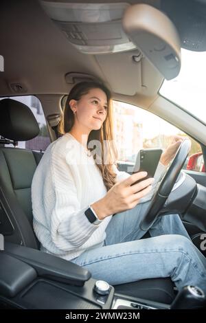 Jeune femme conduisant une voiture et utilisant l'application smartphone pour afficher une carte montrant l'itinéraire de voyage Banque D'Images