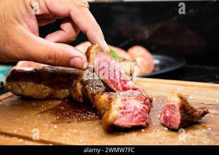 Une main ramassant rare cuisson picanha viande steak bœuf. Banque D'Images