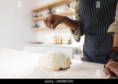 Femme afro-américaine dans le tablier cuit dans une cuisine lumineuse. Banque D'Images