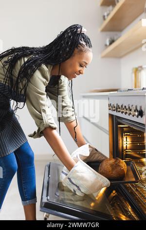 Une jeune femme afro-américaine sort une miche de pain d'un four Banque D'Images