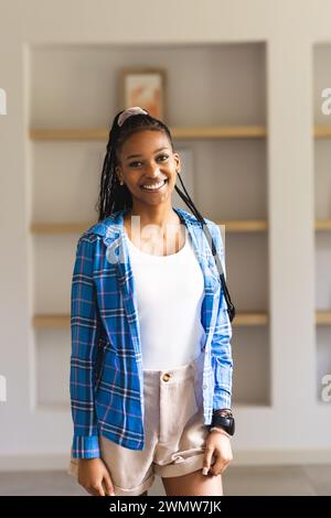 Une jeune femme afro-américaine sourit avec éclat, vêtue d'une chemise à carreaux bleus et d'un haut blanc Banque D'Images