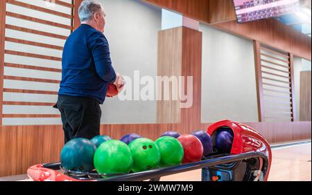 Homme senior choisissant boule de bowling de rack à la piste de bowling, s'engageant dans des loisirs actifs. Banque D'Images