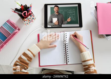 E-learning. Fille prenant des notes pendant la leçon en ligne à la table à l'intérieur, vue de dessus Banque D'Images