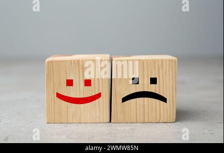 Cubes en bois avec des visages heureux et tristes sur la table grise Banque D'Images