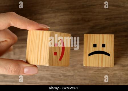 Femme choisissant un cube avec un visage heureux au lieu d'un autre avec triste à la table en bois, vue de dessus Banque D'Images