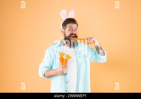 La carotte se compose de vitamines. Heureux et en bonne santé. Le lapin de Pâques tient des carottes. Les oreilles de lapin d'homme barbu tiennent les légumes. Alimentation saine. Régime végétarien Banque D'Images