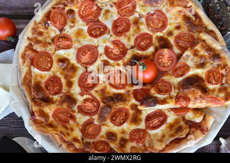 Pizza Margherita maison fraîche servie sur une table en bois rustique. Tranche de pizza, tomates cerises rouges, fromage mozzarella, poivre mill. Banque D'Images