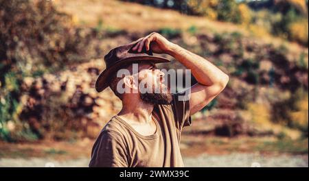 Style cow-boy. Beau jeune homme ajustant son chapeau de cow-boy. Des cowboys en chapeau. Beau macho barbu. Homme non rasé cow-boys. Cow-boy américain. Cuir Banque D'Images