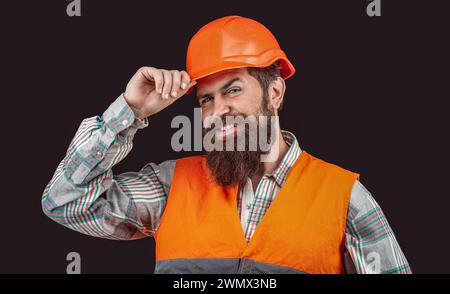 Heureux homme barbu porte un casque isolé sur fond noir. Ingénieur ou architecte sourit. Construction, bonheur, développement, concept de profession Banque D'Images