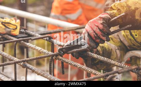 Un travailleur utilise du fil de liage en acier pour attacher des tiges d'acier aux barres de renfort en gros plan. Structures en béton armé - fabrication d'une cage d'armature en acier f Banque D'Images